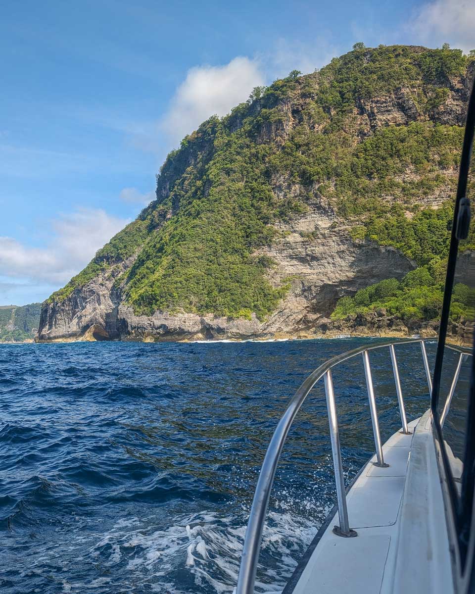 View from a boat approaching Nusa Penida’s cliffs with bright green water near shore - travel photo